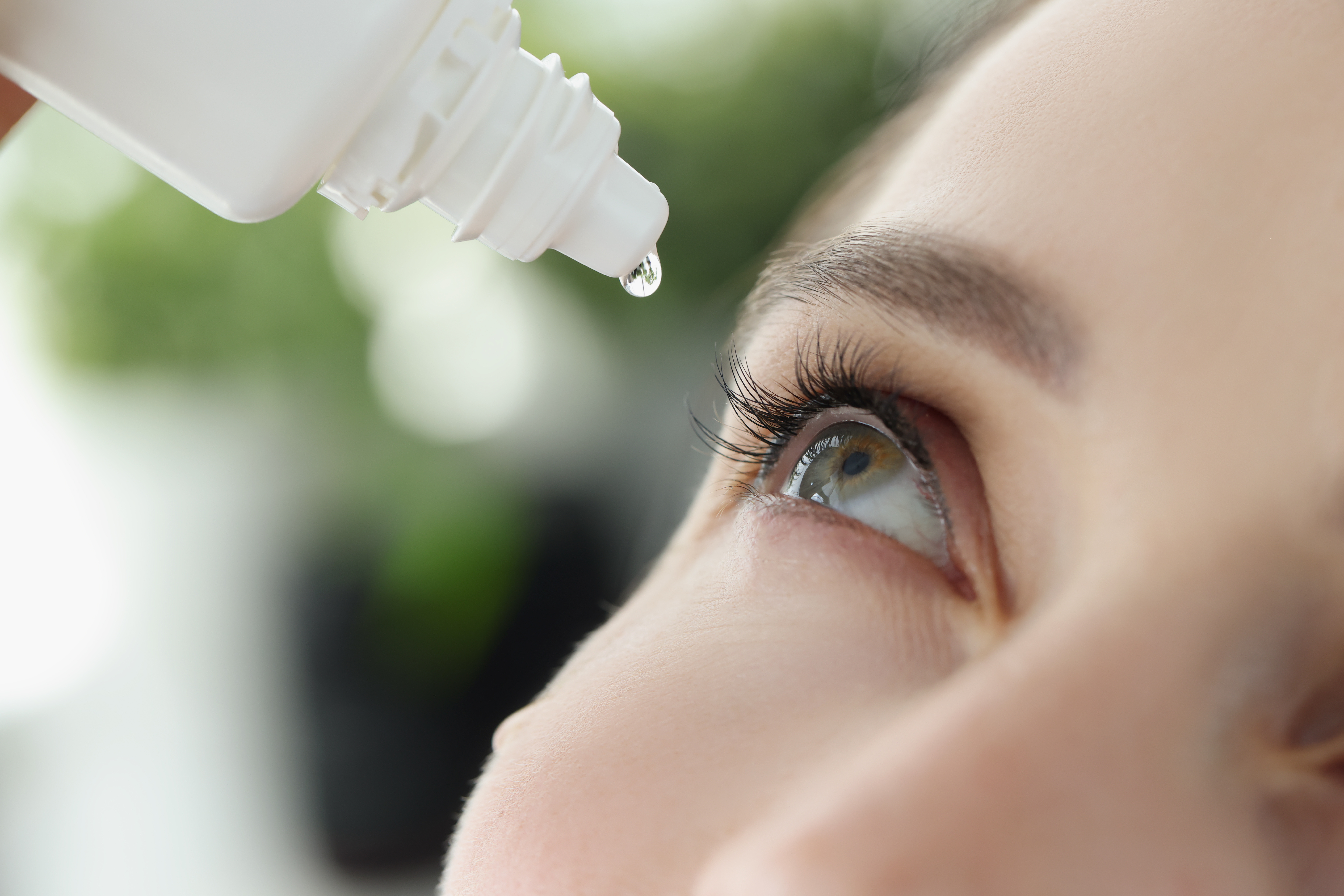 Woman drips eye drops into eye for allergies closeup