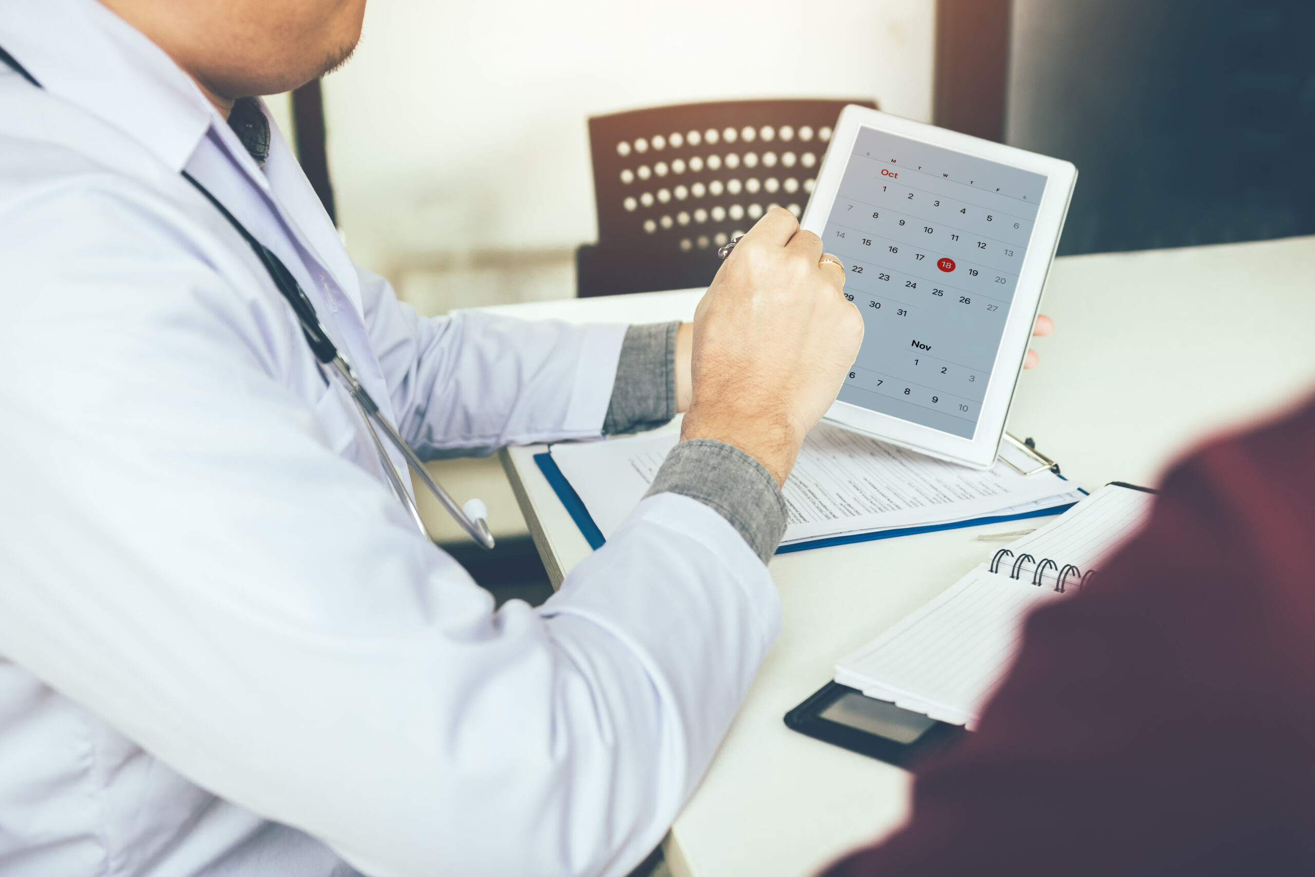 Doctor holding tablet and pointing on calendar appointment reminder to patient.