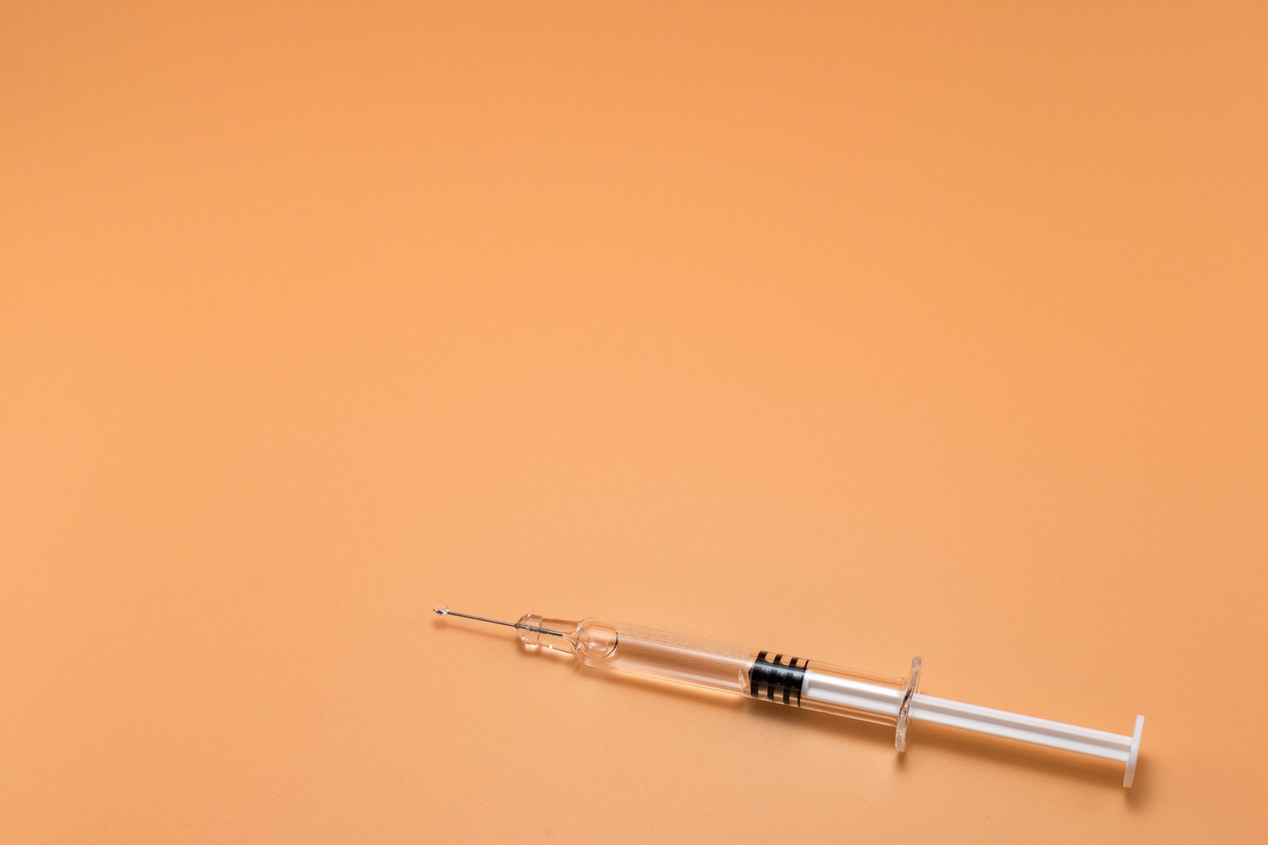 Small full syringe with needle on peach background. Copy Space.